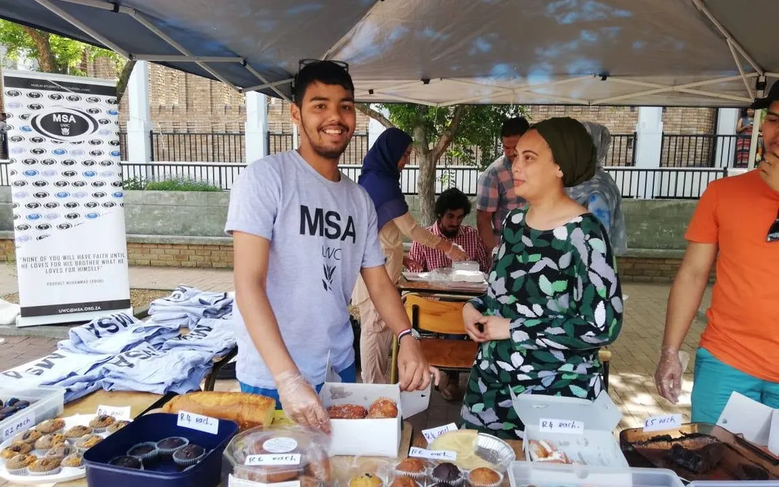 MSA UWC students selling cakes and muffins at a bake sale stall under a gazebo