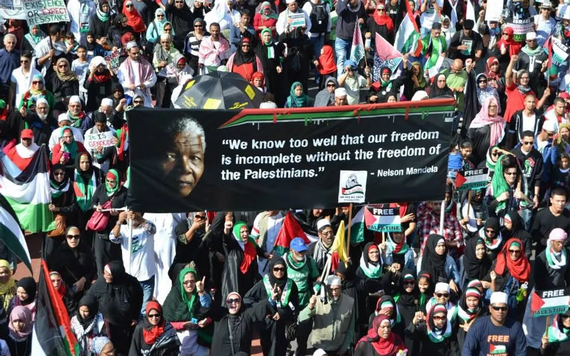 A crowd marching for Palestine behind a banner quoting Nelson Mandela: our freedom is incomplete without the freedom of the Palestinians